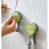 A hand installs a green suction cup hook onto a white surface, demonstrating the product's reusable and removable nature.