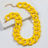 A yellow matte acrylic chain necklace with a gold-tone clasp laid on a white box.
