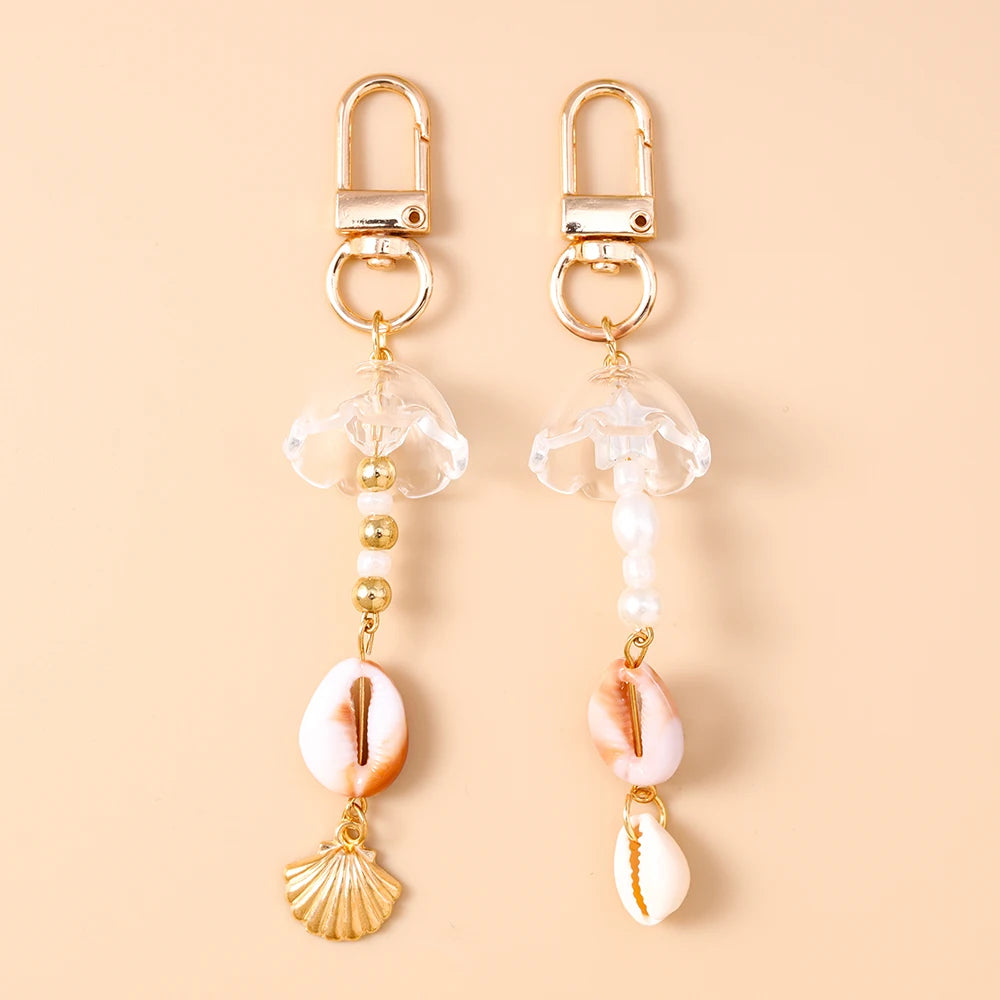 A pair of gold-toned starfish keychains with clear resin and pearl accents displayed on a beige background.