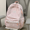 A pink polka dot nylon travel backpack with a laptop compartment resting on a gray chair.