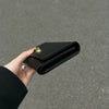 A hand holds a black leather compact women's card holder wallet.