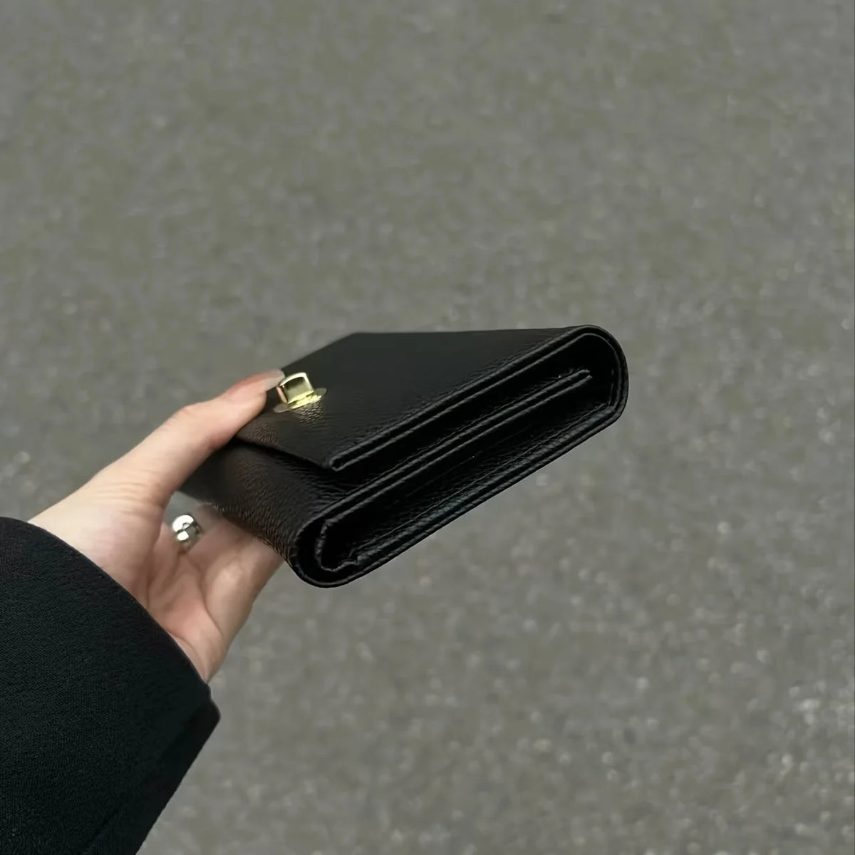 A hand holds a black leather compact women's card holder wallet.