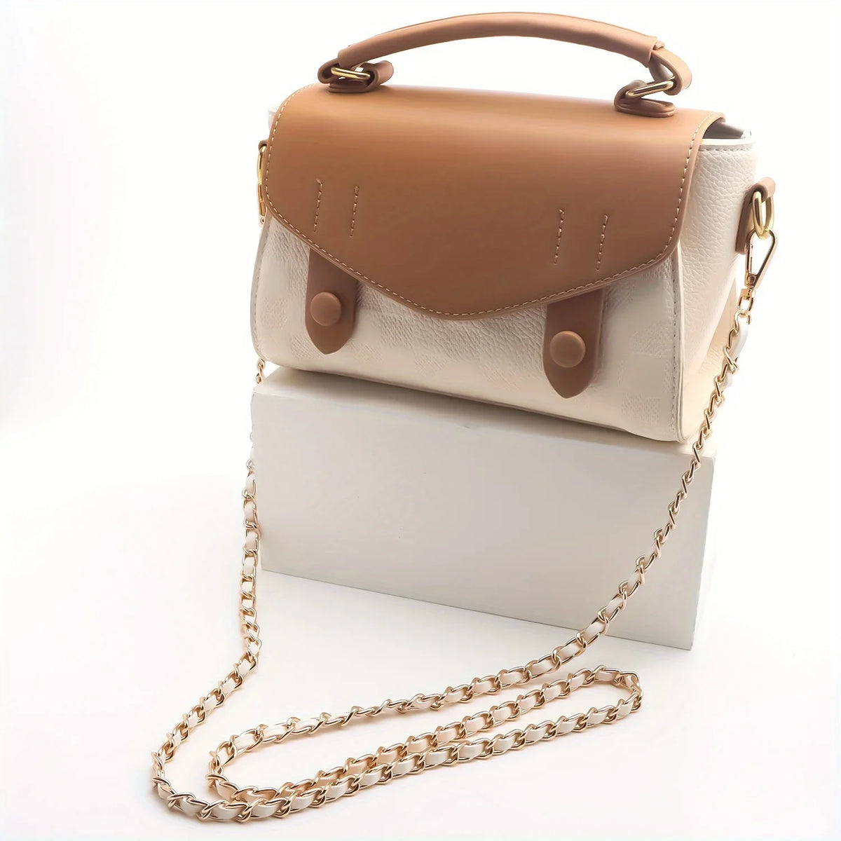 Tan und cremefarbener Leder-Crossbody-Tasche mit goldfargener Kettchenriemen auf einer weißen Box