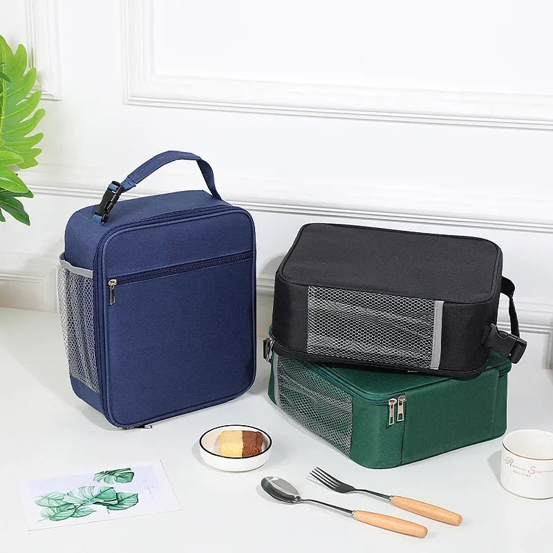Dunkelblaue isolierte Oxford-Stoff-Lunchtasche neben einer schwarz-grünen Lunchtasche und Besteck.