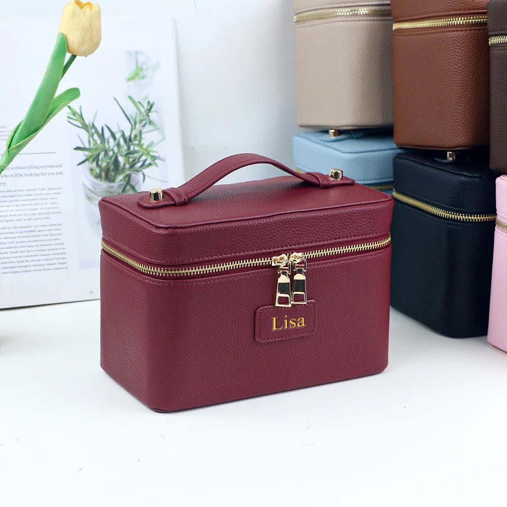 A maroon PU leather makeup bag with gold zippers and a leather tag reading Lisa, displayed next to other colored bags.