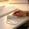 A hand places cat-shaped keycaps onto a white plastic base with a white lanyard on a desk.
