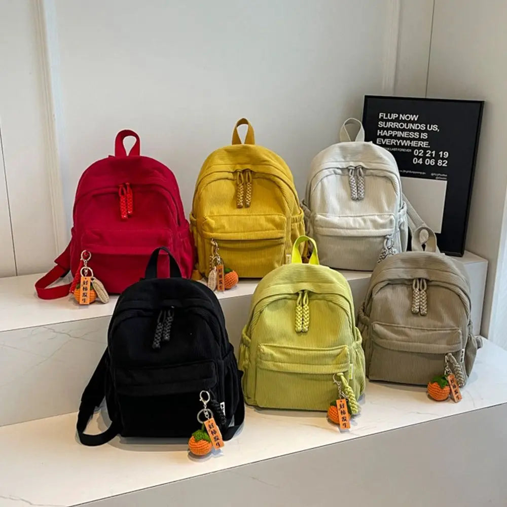 A collection of lightweight corduroy daily backpacks in red, yellow, beige, and olive green displayed on a white surface.