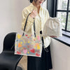 A woman holds a clear plastic shoulder bag with heart-shaped designs and a beige fabric bag next to a window.