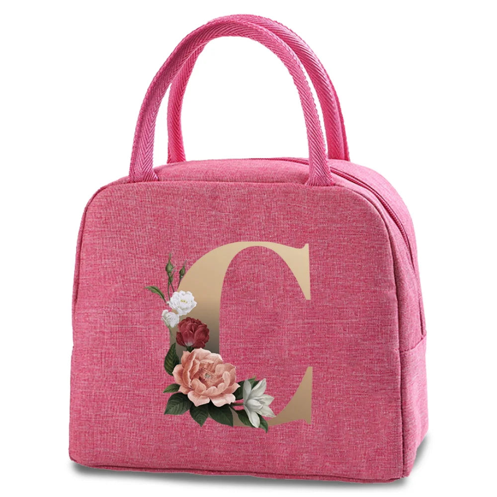 A pink insulated canvas lunch bag featuring a large gold letter C and floral accents.