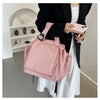 A person holds a pink nylon shoulder bag against a white dress in a bright indoor setting.