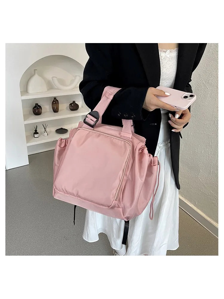 A person holds a pink nylon shoulder bag against a white dress in a bright indoor setting.
