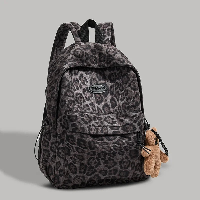 A dark gray leopard print backpack with black straps and a small teddy bear charm.