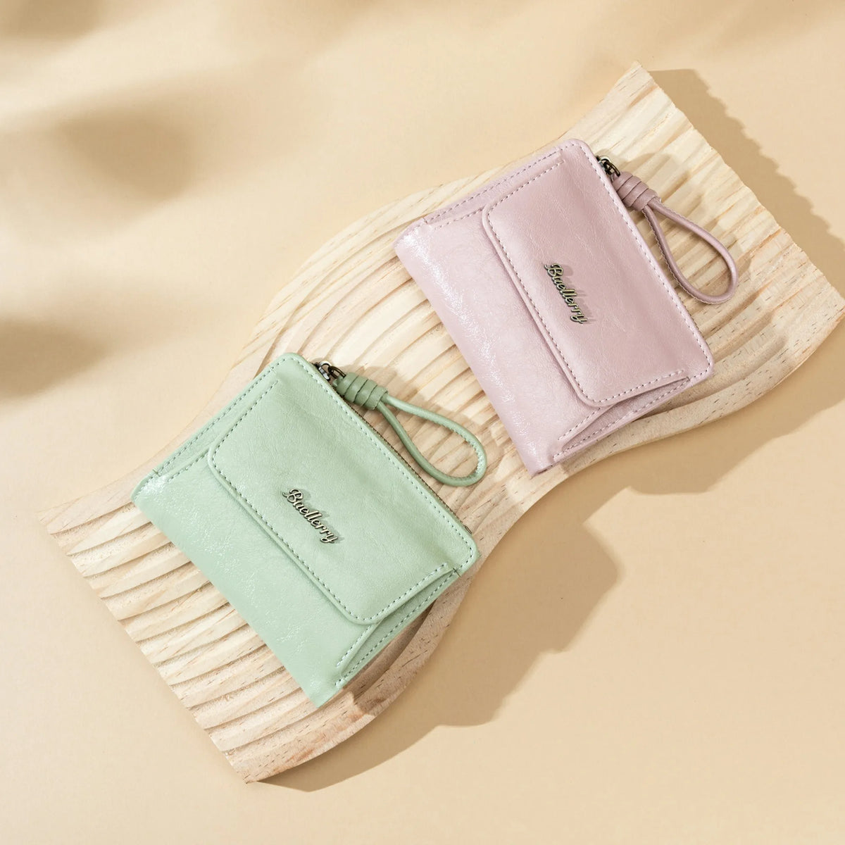 A light pink leather mini wallet with a cord is placed on a wooden surface.