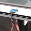 A silver hook with a blue marble design is attached to a white desk, hanging from a brown leather strap.