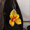 A yellow orchid flower keychain hanging from a zipper pull on a dark brown backpack.