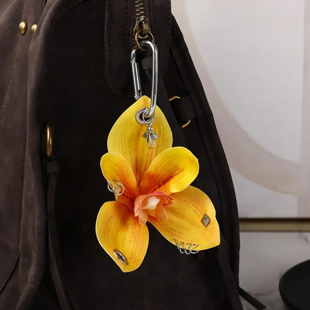 A yellow orchid flower keychain hanging from a zipper pull on a dark brown backpack.