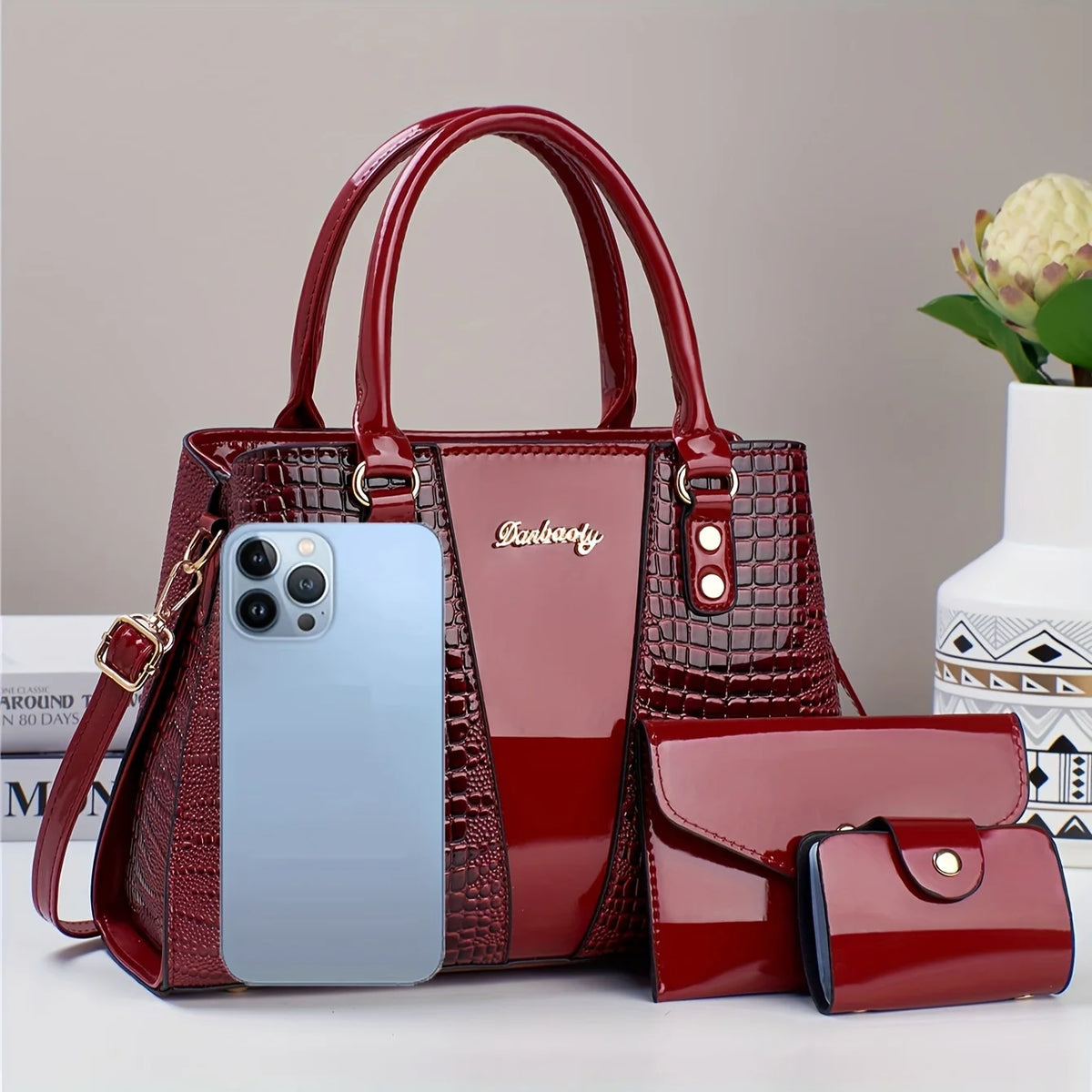 Set de bolso y clutch de cocodrilo de cuero patentado color granate, exhibido sobre una superficie blanca.
