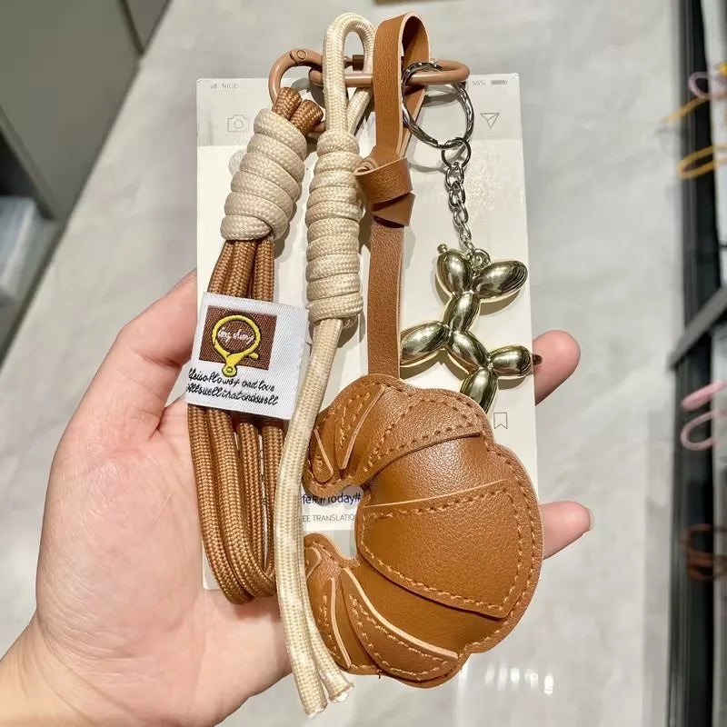 A brown leather croissant shaped keychain with a gold chain and beige lanyard attached to a card.