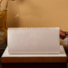 A rectangular satin evening clutch in a pale pink color resting on a wooden surface.