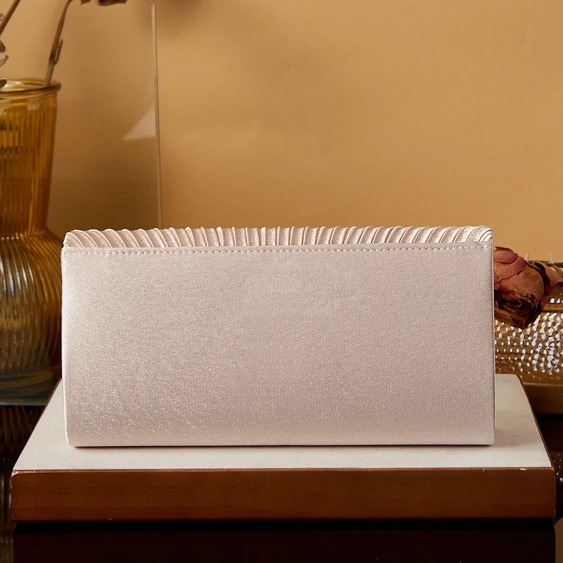 A rectangular satin evening clutch in a pale pink color resting on a wooden surface.