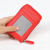 A hand holds a red textured card holder wallet with a clear plastic slot and a silver zipper pull.