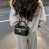 A woman is holding a black woven crossbody bag with a silver chain strap against a gray background.