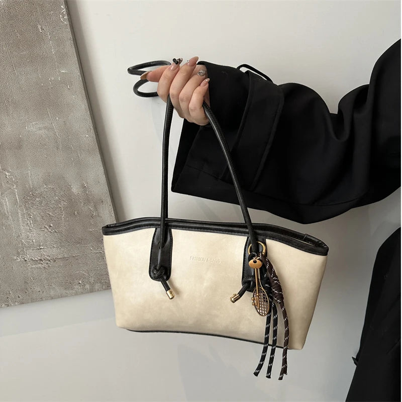 A black blazer holds a cream leather tote bag with gold hardware and a leather strap.