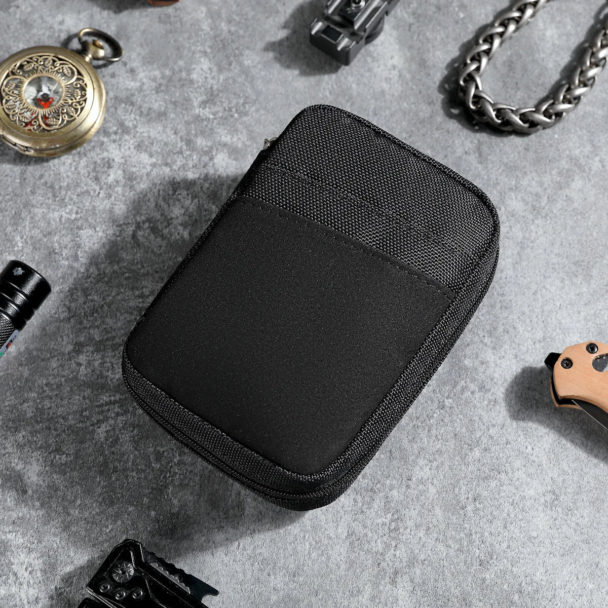 A black padded pouch for organizing multi-tools and outdoor gear placed on a gray surface.