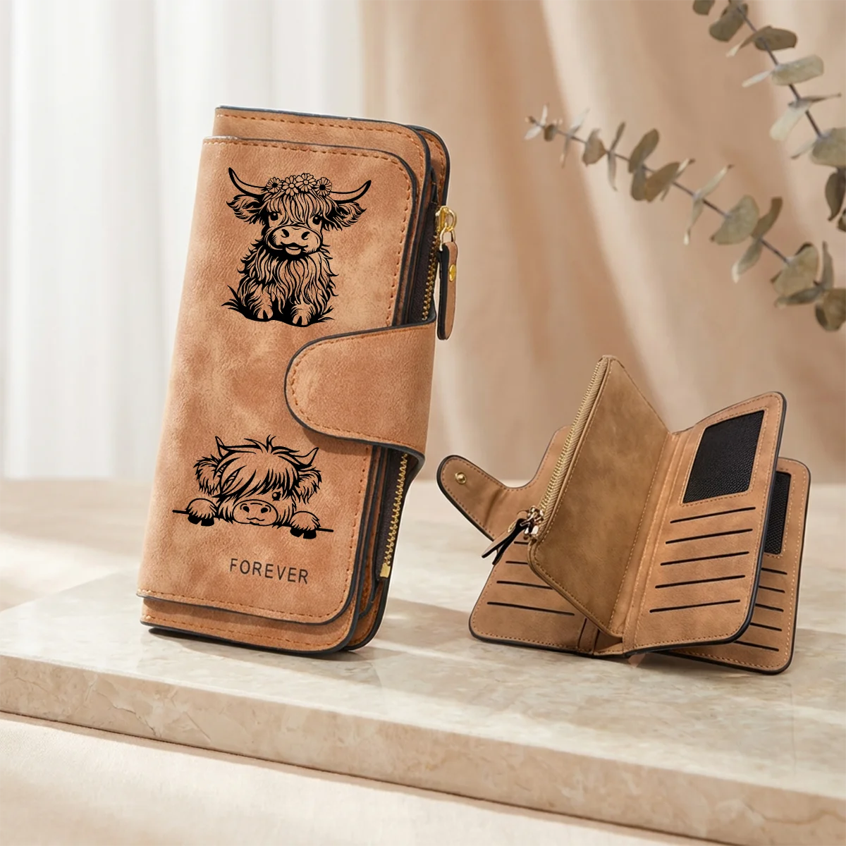Cartera de cuero PU color caramelo con temática de vaca y cierre de cremallera, apoyada sobre una superficie clara.