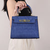 A woman holds a blue crocodile pattern tote bag with gold hardware against a light background.