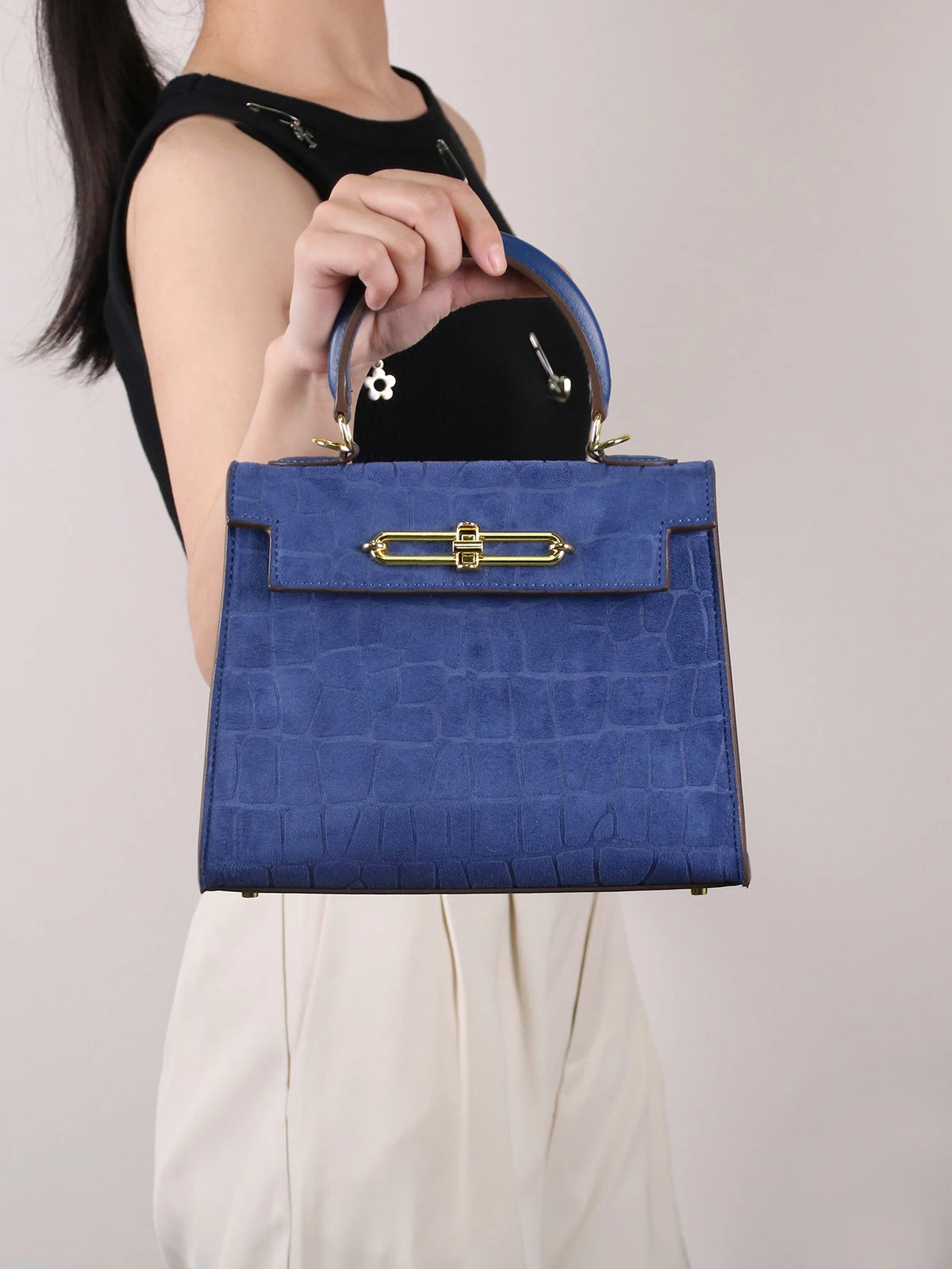 A woman holds a blue crocodile pattern tote bag with gold hardware against a light background.