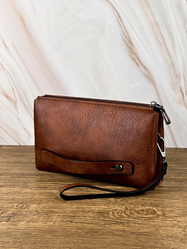 A brown leather retro men's clutch wallet bag resting on a wooden surface.