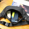 Un sac bandoulière noir de créateur ouvert, montrant un smartphone et une bouteille blanche à l'intérieur.