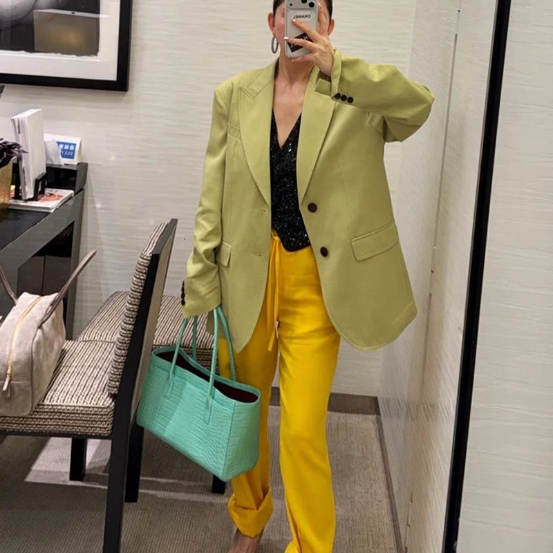 A woman wearing a light green blazer and yellow pants holds a mint green tote bag.