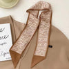 Foulard pour les cheveux en soie beige avec texte répétitif sur tissu marron, exposé sur fond neutre.