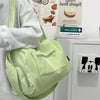 A light green canvas crossbody travel tote bag is shown next to a gray sweatshirt and a framed sign.