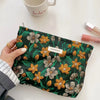 A dark green cosmetic pouch with a floral pattern rests on a white surface next to a ceramic mug.