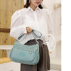 A woman wearing a white shirt and brown skirt holds a mint green waterproof nylon crossbody shoulder bag.