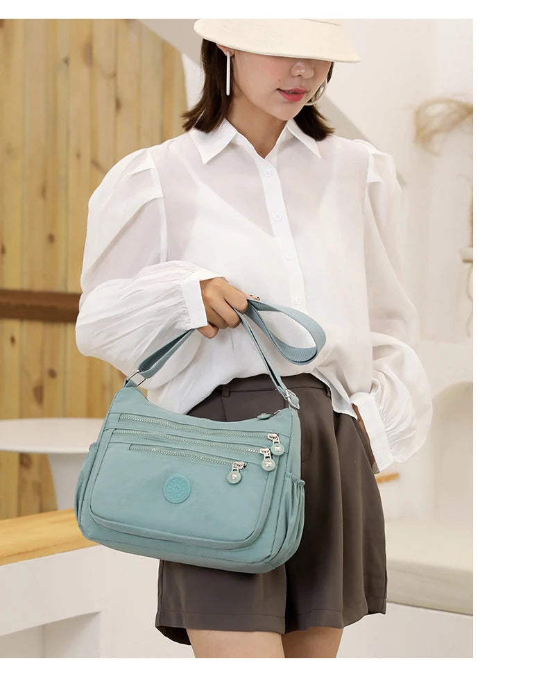 A woman wearing a white shirt and brown skirt holds a mint green waterproof nylon crossbody shoulder bag.