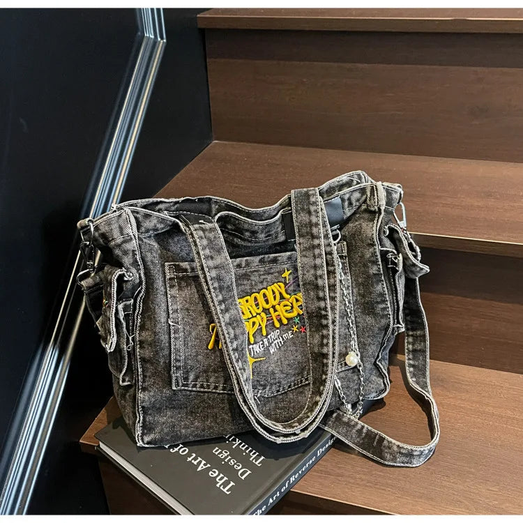 A dark gray denim crossbody bag with a flap and strap resting on a wooden surface.