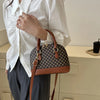 A woman holds a brown leather fashion shell shoulder crossbody bag with a checkered pattern against a light background.