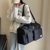 A person wearing a light gray sweatshirt holds a black quilted travel duffle bag over their shoulder.