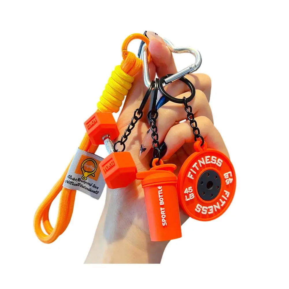 A hand holds an orange fitness keychain featuring a dumbbell and kettlebell charm.