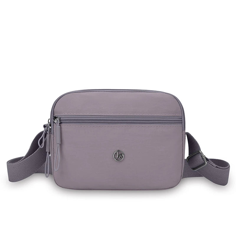 A mauve nylon crossbody bag with a zipper and adjustable strap is shown against a white background.