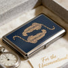 A dark blue metal card holder featuring a gold leopard print design resting on a light fabric.