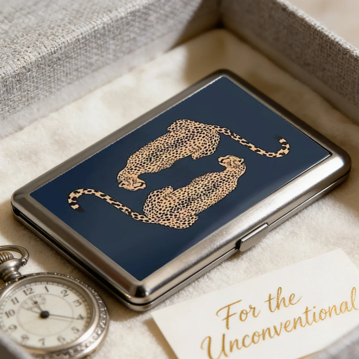 A dark blue metal card holder featuring a gold leopard print design resting on a light fabric.