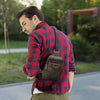 A man wearing a red plaid shirt and olive pants is carrying a brown genuine leather men's crossbody bag.