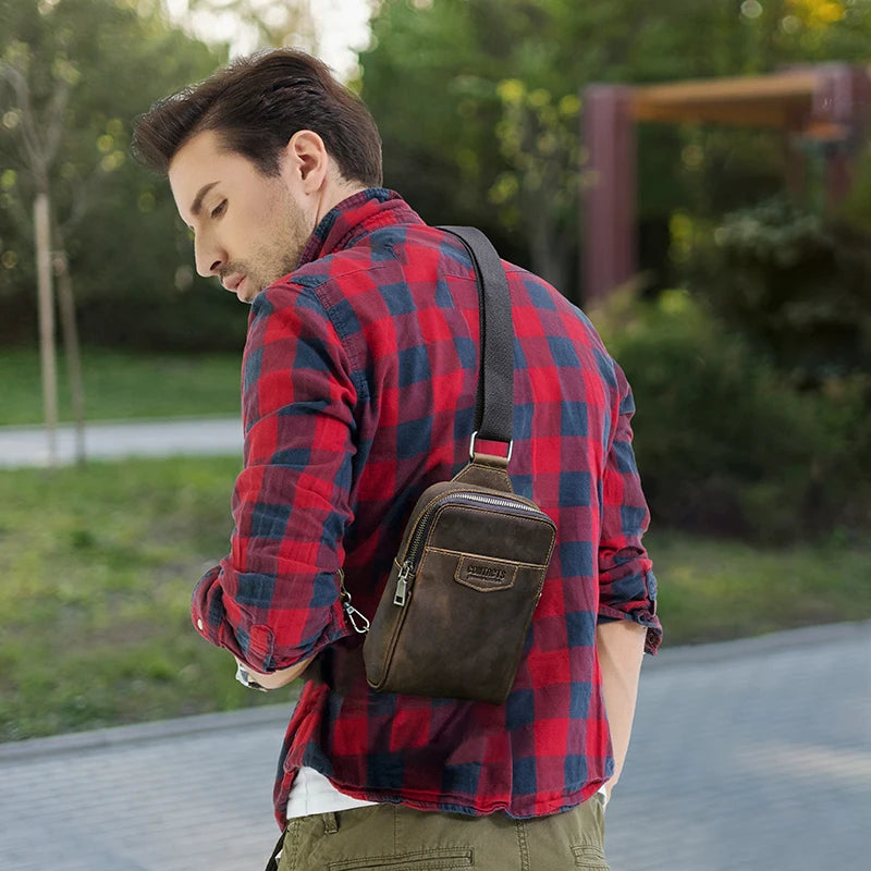 A man wearing a red plaid shirt and olive pants is carrying a brown genuine leather men's crossbody bag.