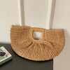 A woven rattan half-moon beach handbag displayed against a white wall.