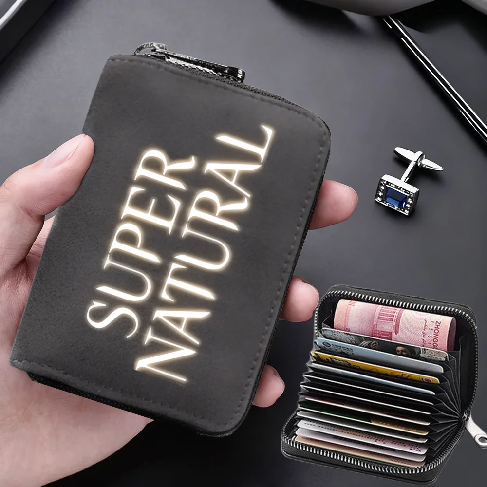 A dark gray compact card wallet with glowing text on the cover is held in a hand next to a separate black card holder.